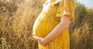 femme enceinte portant une robe jaune à fleurs, debout, se touchant le ventre et faisant face à son côté droit près d'un champ brun pendant la journée